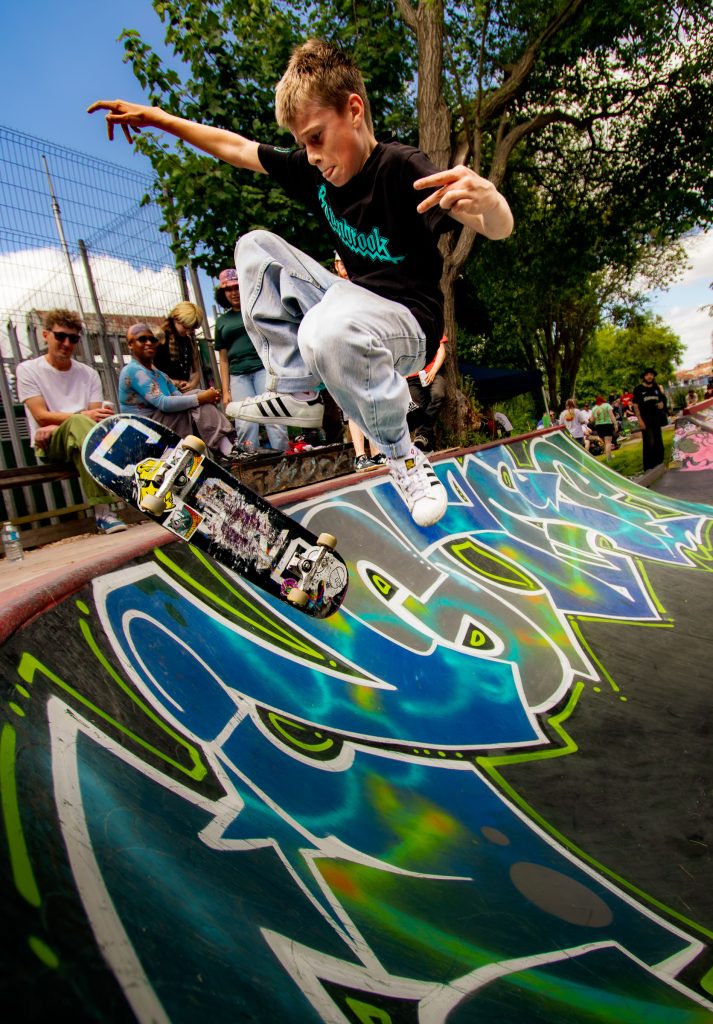 Young skateboarder performing a trick over colourful graffiti at an outdoor skatepark captured with a wide-angle lens.