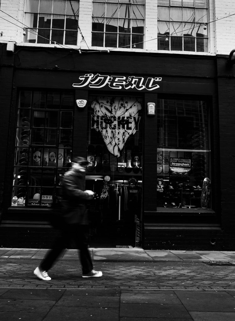 Black and white street photograph of a pedestrian walking past an independent skateboard shop in Birmingham.