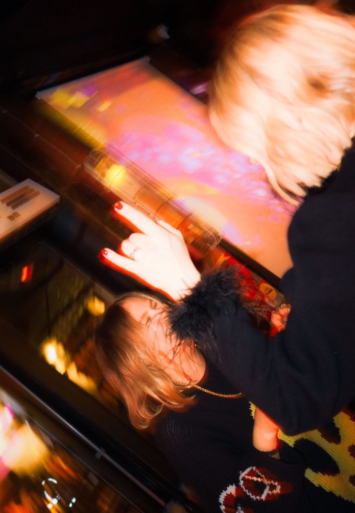 Creative motion blur photograph of people interacting around an illuminated arcade machine inside a nightclub.