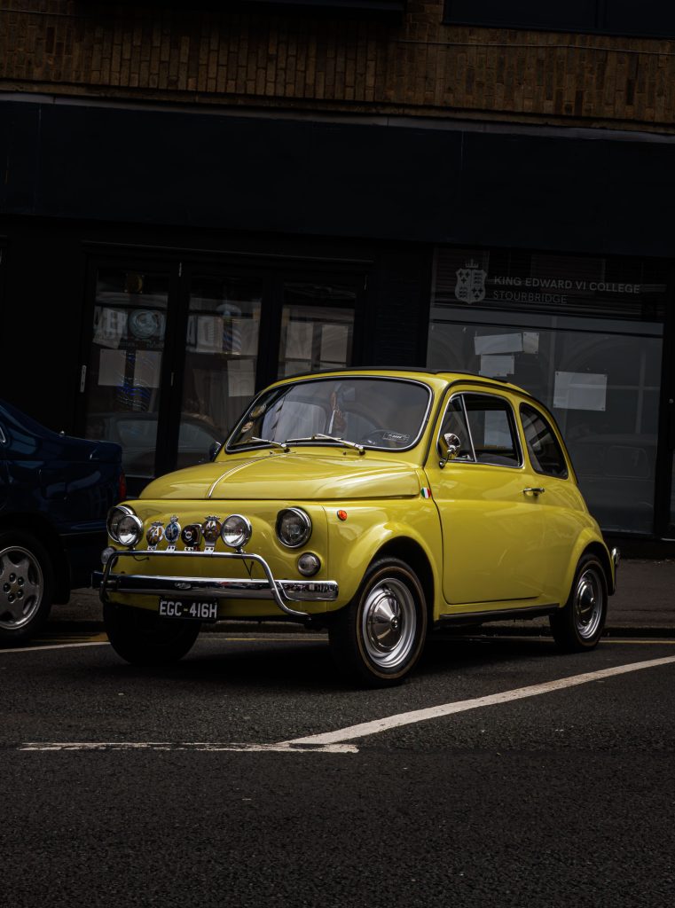 Vintage yellow Fiat 500 parked on a city street photographed in natural light.