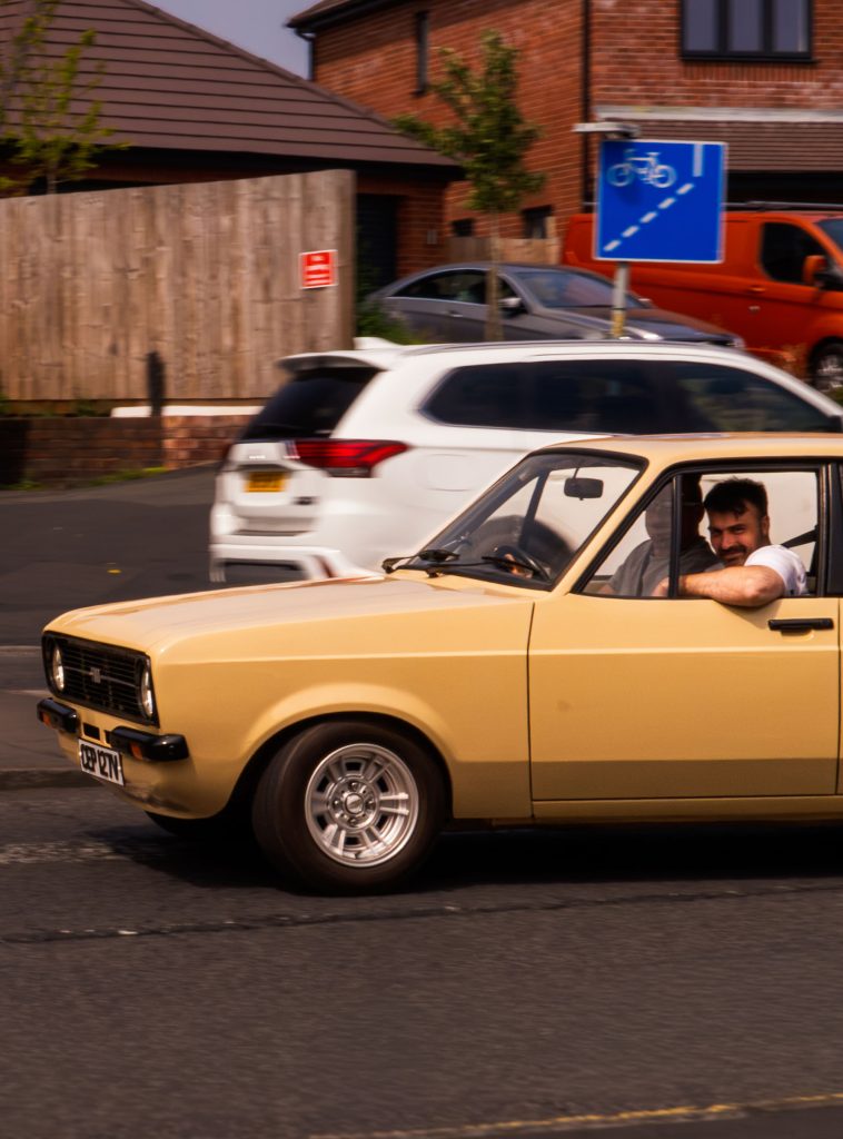 Street photograph of a classic beige car with the driver looking directly towards the camera.